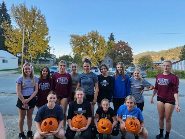 the girls varsity volleyball team smiling, four of them holding jack-o'-lanterns